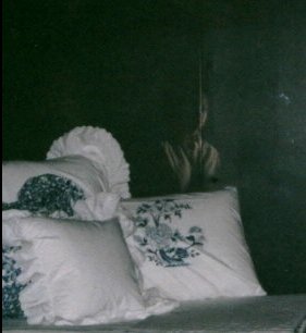 Foto de alguns travesseiros na penumbra e a imagem de uma pessoa aparece atrs deles.