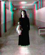 Foto de uma menina de vestido preto de pé em um corredor segunando uma boneca