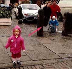 Foto de uma criança de rosa caminhando e duas pessoas atras, do lado direito da foto
